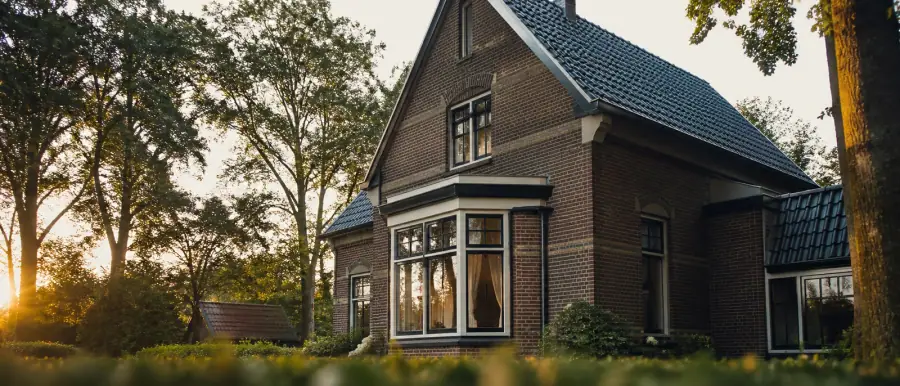 Jaren-30-gevel met erker, siermetselwerk en een steil pannendak, tussen hoge bomen